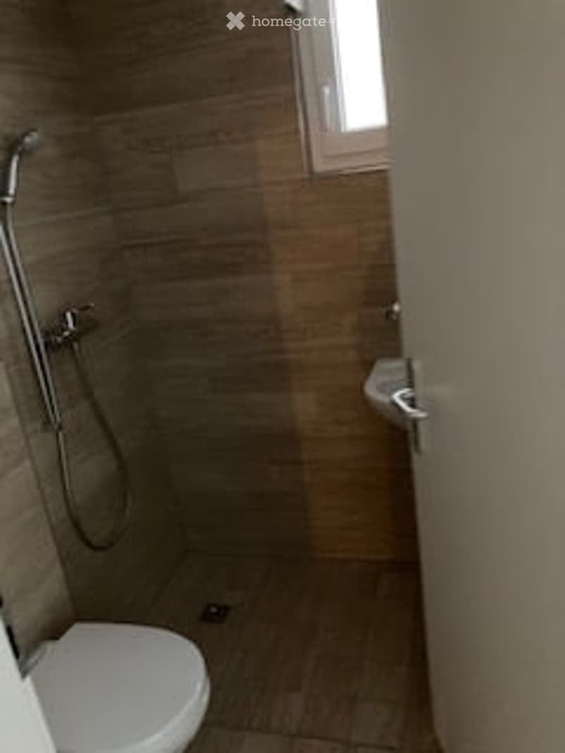 Modern bathroom with a toilet, shower, and a small window above the shower area.