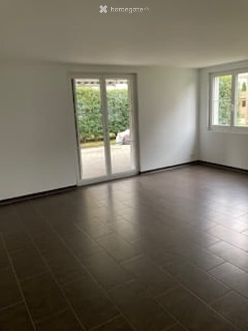 Empty room with white walls, dark tiled floor, large sliding glass door leading to outdoor area, and a window on the opposite wall.