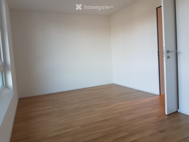 Empty room with light-colored walls and wooden flooring, featuring a single door and a window on one side.