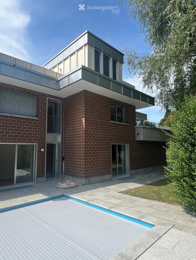 Modern two-story house with brick and concrete exterior, large windows, balconies, and a swimming pool in the courtyard.