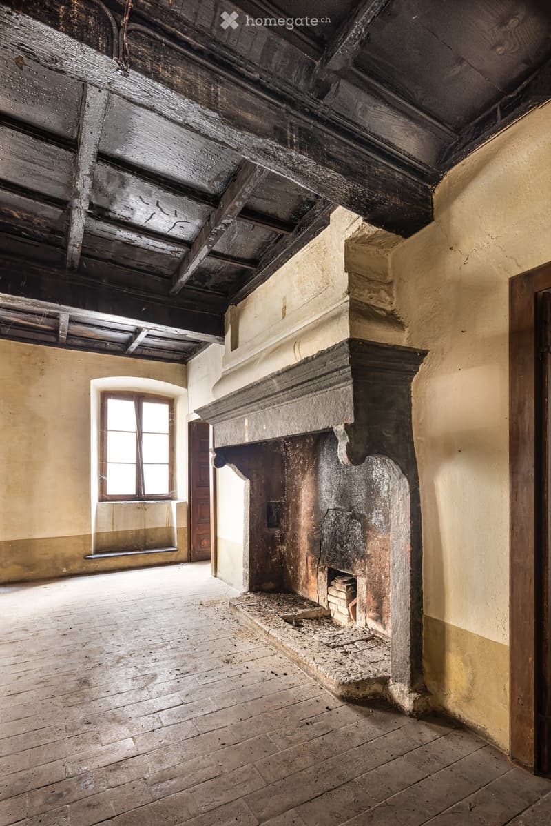 Empty room with exposed wooden beams, stone fireplace, wooden floor, and a window with wooden frame.
