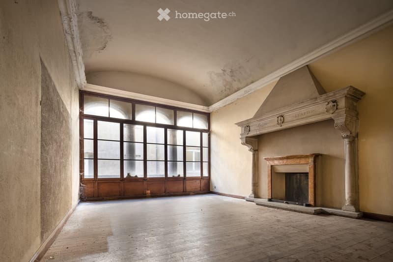 Empty room with wooden flooring, large arched windows, and a fireplace with decorative mantel.