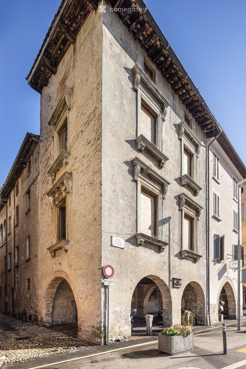 Historic stone building with arched entrances and decorative stonework, located on a narrow cobblestone street.