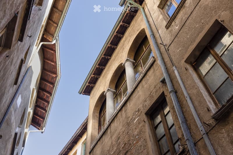 Close-up view of an old stone building facade with arched windows, wooden shutters, and visible pipes.