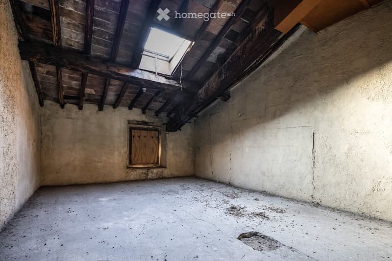 Empty attic space with exposed wooden beams, concrete floor, and small skylight window.