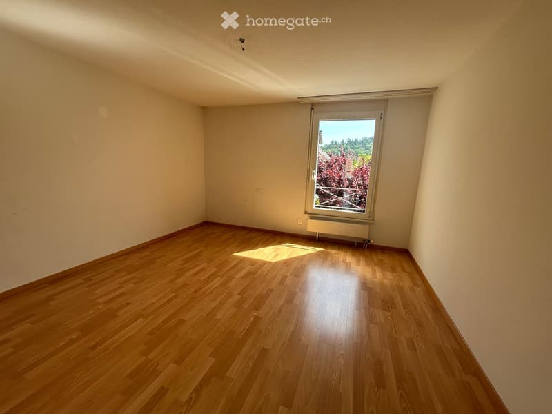 Empty room with wooden flooring, white walls, and a large window with blinds. Natural light streams in, illuminating the space.