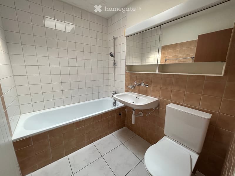 Modern bathroom with white tiled walls, a bathtub, a toilet, a sink, a mirror, and a shower head.