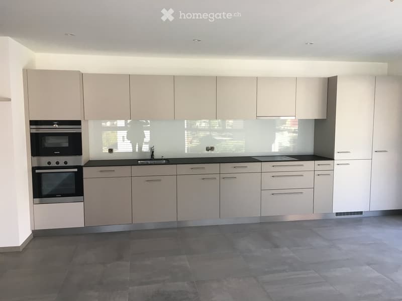 Modern kitchen with light grey cabinets, stainless steel oven, and a black countertop.