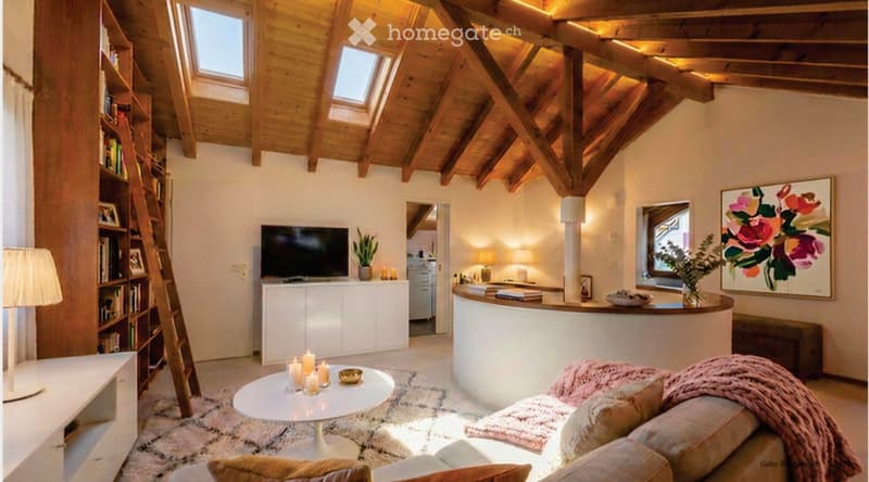 Cozy living room with exposed wooden beams, skylights, a sofa, coffee table, bookshelf, TV, and a kitchen island in the background.