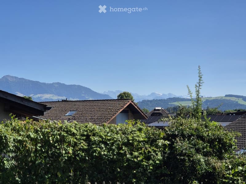A view of a house with a tiled roof, surrounded by greenery and a scenic mountain backdrop.