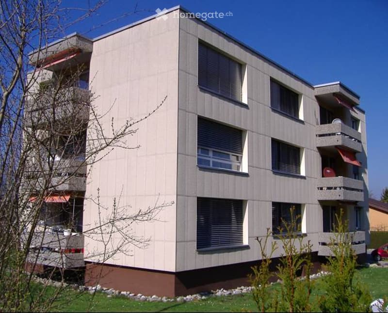 Modern multi-story apartment building with balconies, large windows, and a clean facade.