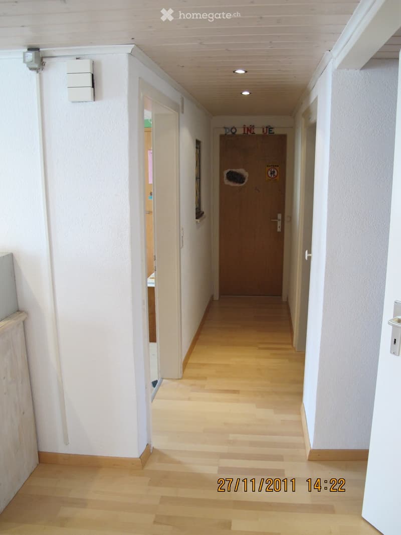 Clean, well-lit hallway with light wooden flooring, white walls, and several doors. A sign on one door reads "DO NOT ENTER."