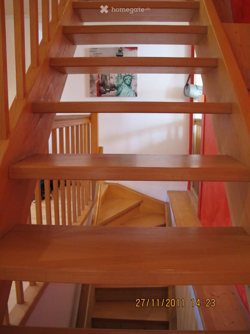 Wooden staircase with handrails and steps, featuring a poster of the Statue of Liberty on the wall.