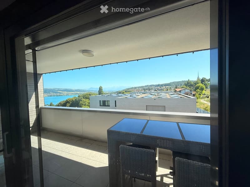 Balcony with a scenic view of a lake and surrounding landscape, featuring a table and chairs.