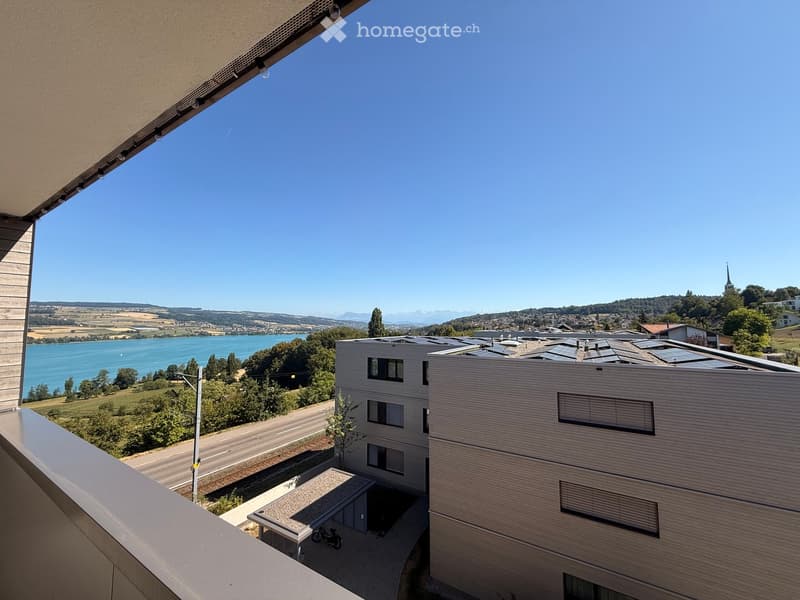 Balcony overlooking a scenic landscape with a lake, distant hills, and modern buildings.