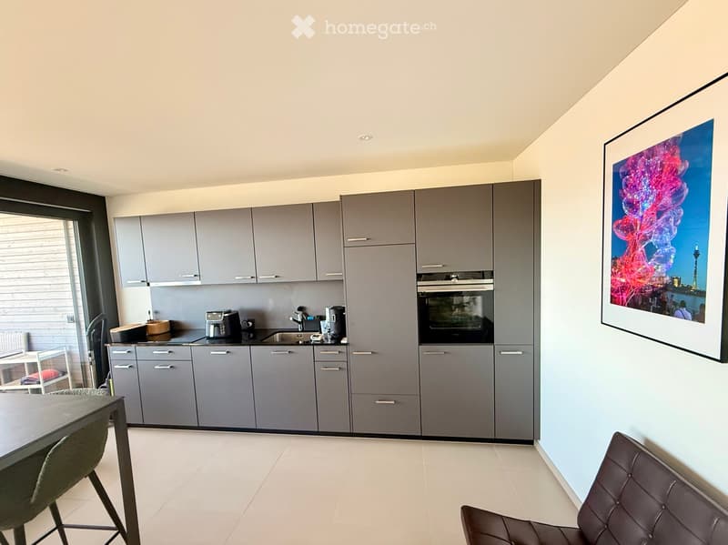Modern kitchen with grey cabinets, stainless steel appliances, a large window, and a dining area with a table and chairs.