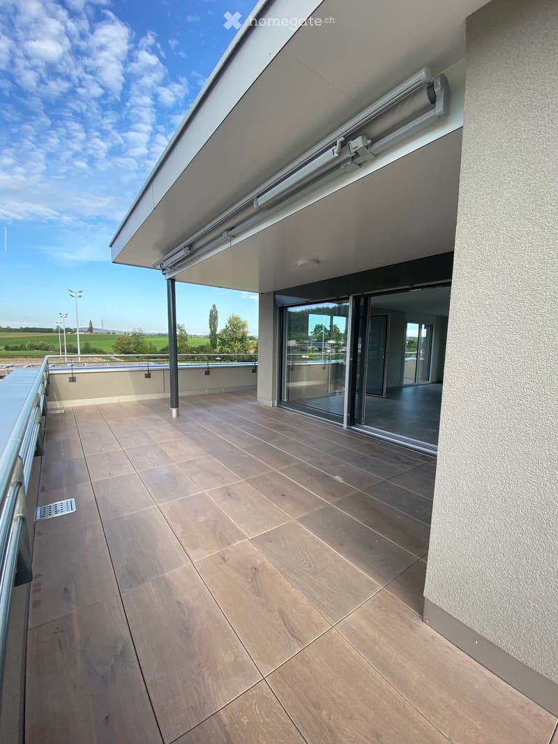 Modern balcony with tiled flooring, glass sliding doors, metal railing, and a retractable awning.
