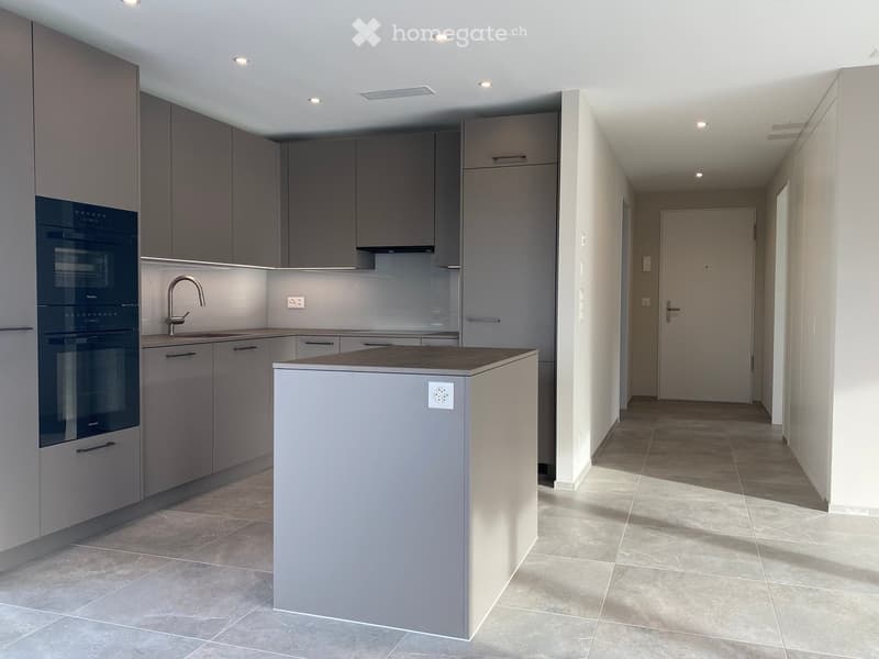 Modern kitchen with grey cabinets, a central island, and a built-in oven. The space features a sleek design with a tiled floor and recessed lighting.