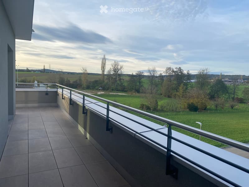 Balcony with tiled floor, metal railing, and scenic view of green fields and trees.