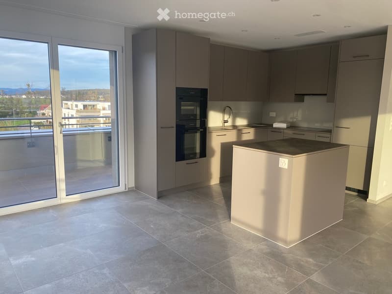 Modern kitchen with grey cabinets, a central island, and a large window offering a scenic view.