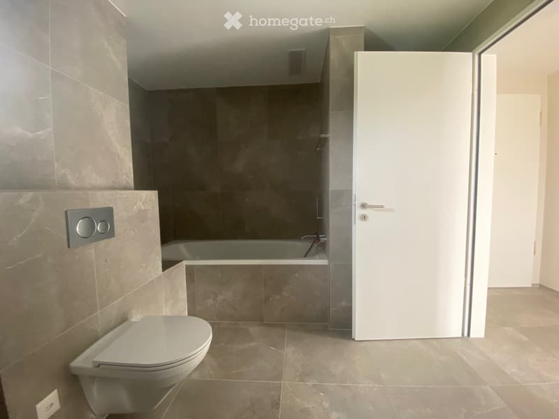 Modern bathroom with a toilet, bathtub, and sleek grey marble tiles on walls and floor. Features a white door and a control panel on the wall.