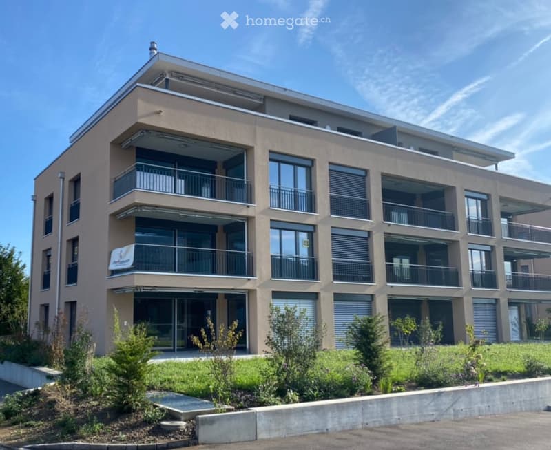 Modern multi-story building with balconies, large windows, and a landscaped entrance area.