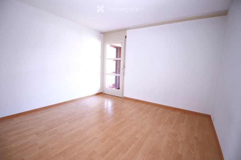Empty room with light wooden flooring, white walls, and a white door with glass panels.