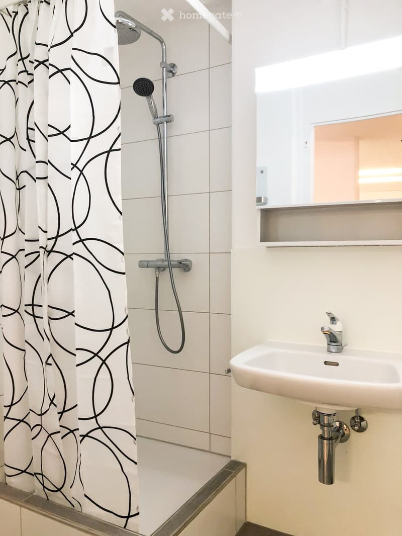 Modern bathroom with a white tiled shower area, a patterned shower curtain, a handheld showerhead, and a white sink with a modern faucet.