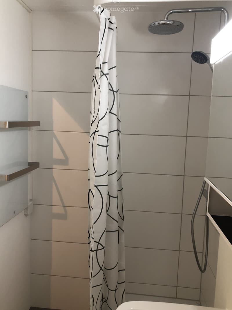 Modern bathroom with tiled walls, a glass shower enclosure, a white shower curtain with black abstract design, a modern showerhead, and a toilet.