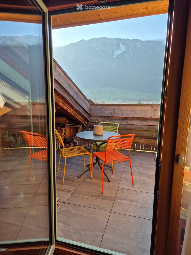 Balcony with a round table, four chairs, and a decorative vase, overlooking a mountain view.