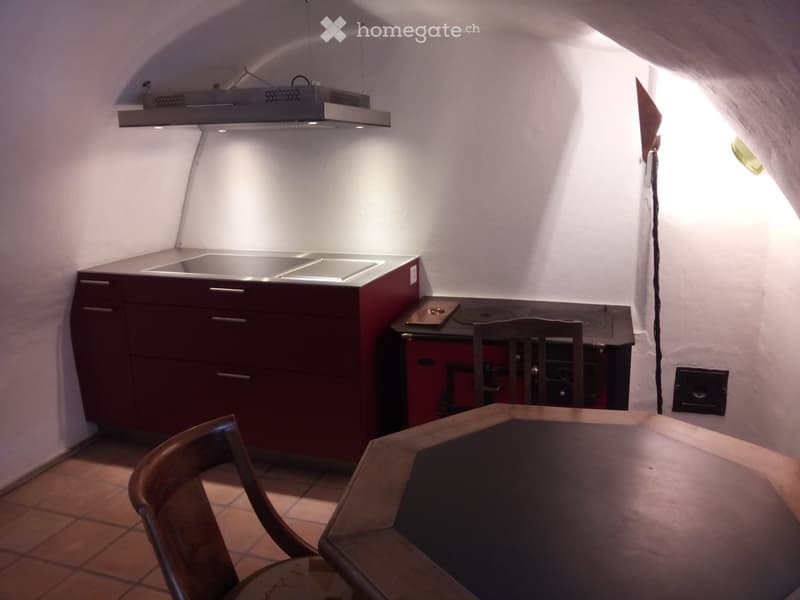 A small, cozy kitchen with a wooden table and chairs, a sink, a stove, and dark red cabinets.