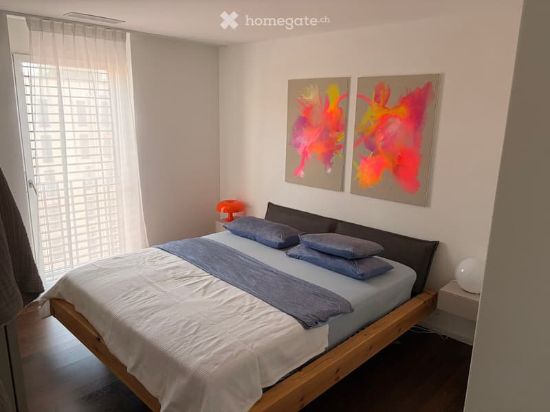 Modern bedroom with a wooden bed, blue bedding, nightstands, and colorful abstract paintings on the wall.