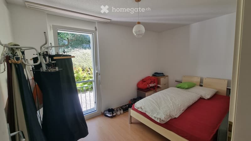 Cozy bedroom with a single bed, nightstand, backpack, shoe rack, and a hanging clothes rack near the window.