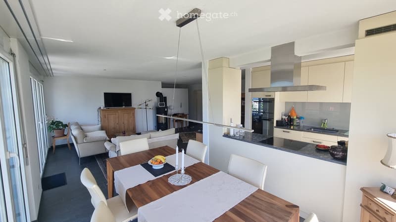 Open-plan living and dining area with a sofa, dining table, and kitchen area featuring modern cabinets and appliances.