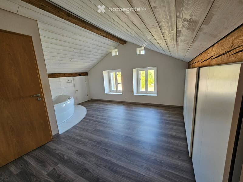Bathroom with wooden flooring, white walls, exposed wooden beams on the ceiling, and a bathtub in the corner.