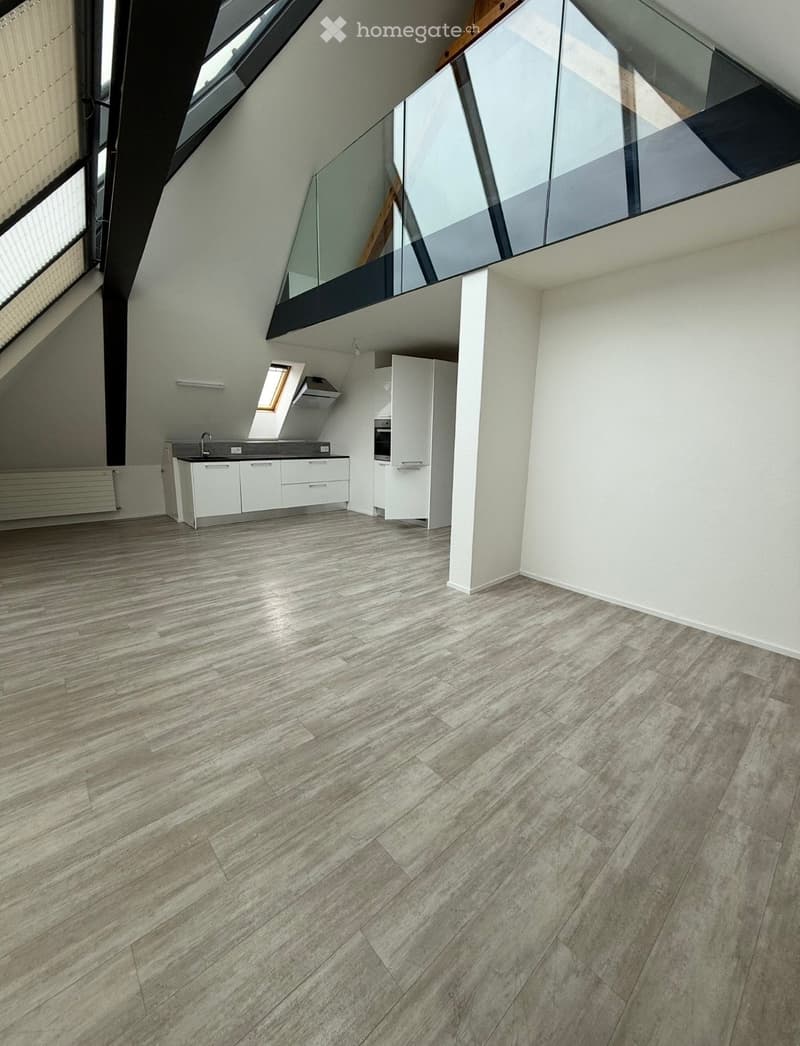 Empty kitchen with white cabinets, a sink, and a modern wooden floor. The space features large windows and a glass balcony overlooking the room.