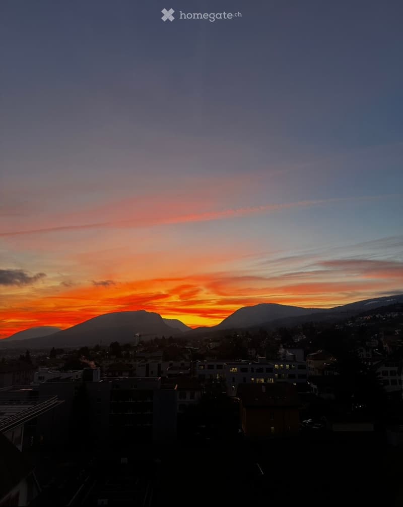 A cityscape view at sunset with mountains in the background and buildings in the foreground.