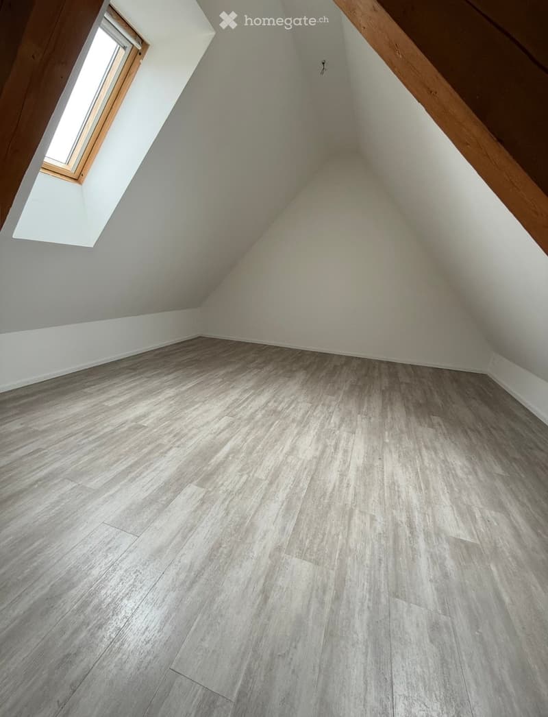 Empty attic space with wooden flooring and a skylight window, featuring exposed wooden beams on the ceiling.