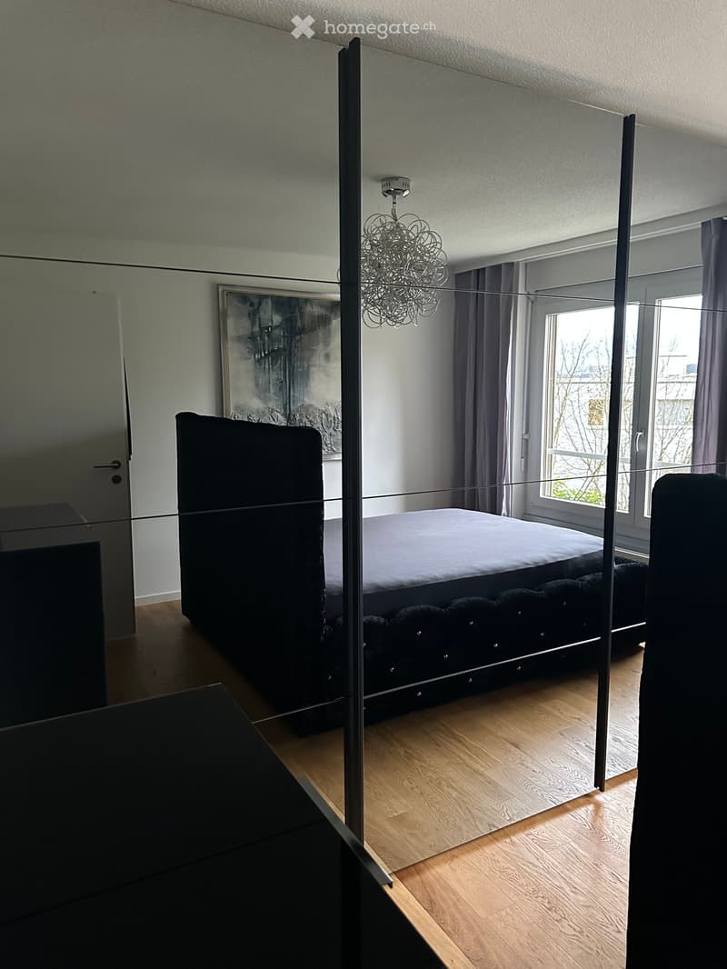 Modern bedroom with a large bed, chandelier, large window with curtains, and a painting on the wall.