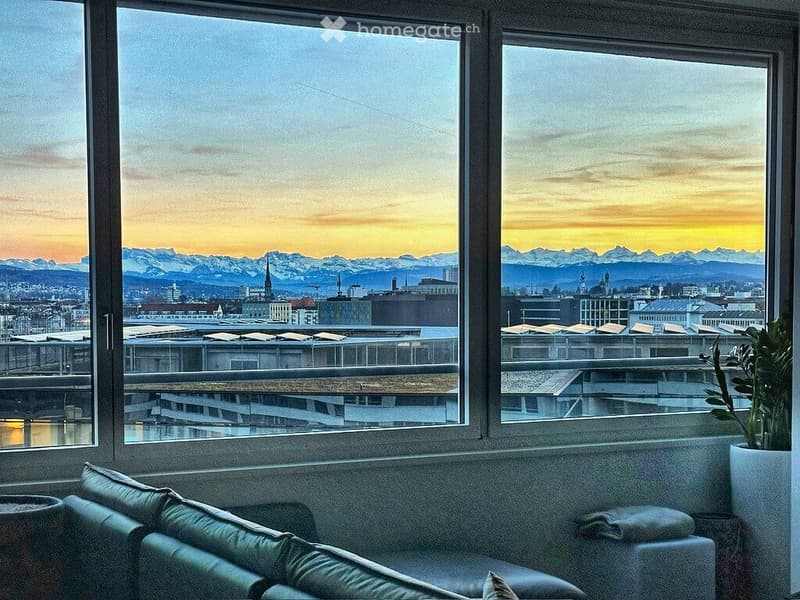 Modern balcony with panoramic city and mountain view, featuring a comfortable sofa and potted plants.