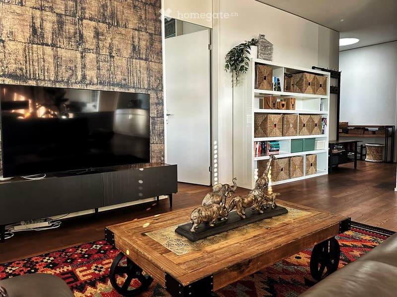 Modern living room with hardwood floors, large television, coffee table with animal statues, bookshelf, and decorative rug.