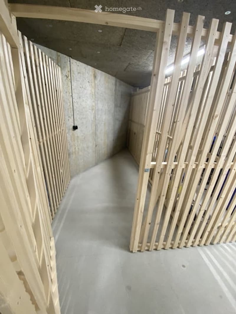 Empty unfinished basement corridor with concrete walls and floor, wooden framing for future walls, and exposed ceiling beams.