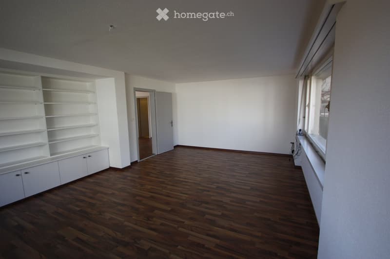 Empty room with wooden flooring, white walls, built-in white shelving unit, and a doorway leading to another room.