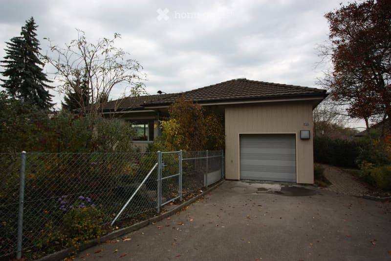 Two-story house with a garage, surrounded by a chain-link fence and trees.