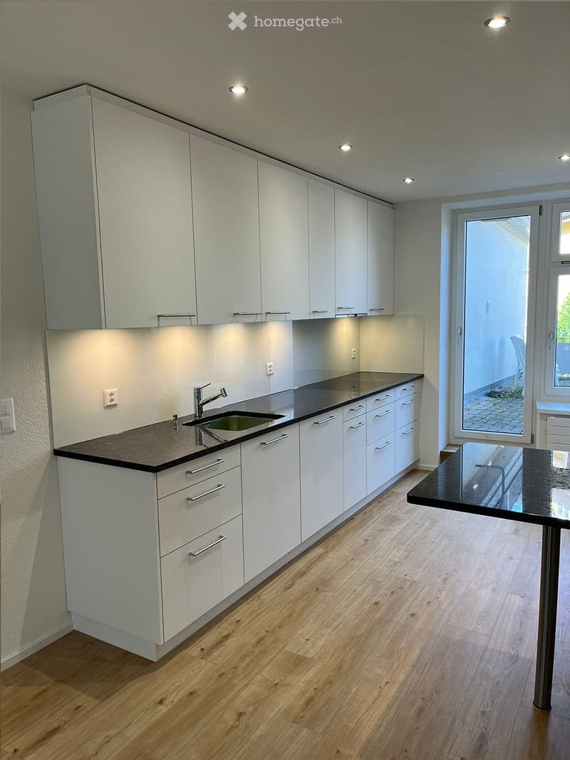 Modern kitchen with white cabinets, dark countertops, a sink, and a small black table near the window.