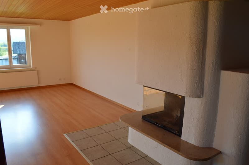 Empty room with wooden flooring, white walls, and a fireplace with a glass front.