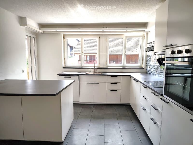 Modern kitchen with white cabinets, black countertops, a central island, and a built-in oven. The space features a large window with a view of the outside.