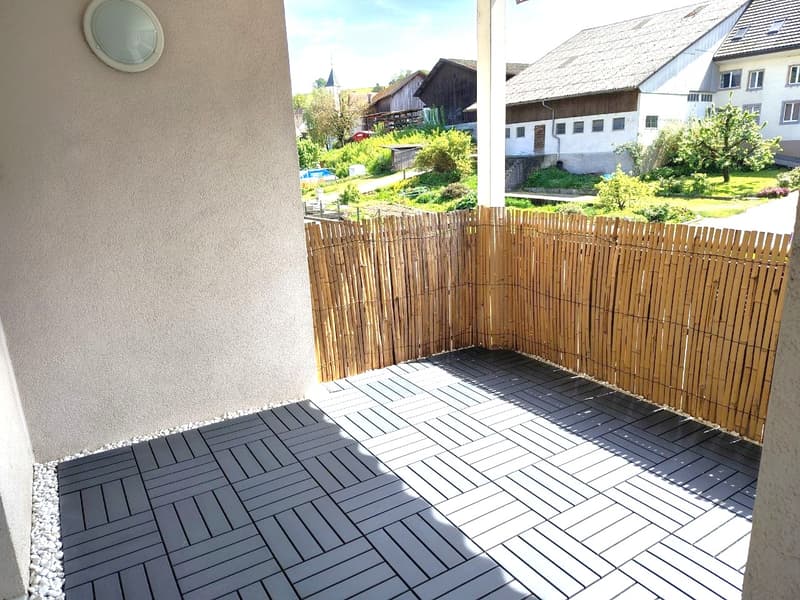 Wooden deck with grey tiles, bamboo fence, and view of neighboring houses and greenery.