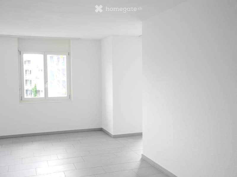 Empty room with white walls, tiled floor, and a single window with a view of a building and greenery outside.