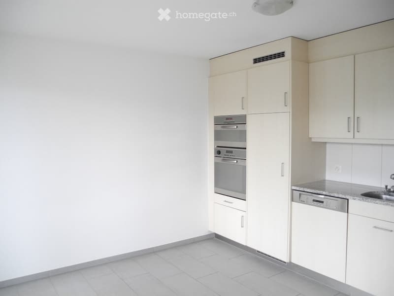 Modern kitchen with white cabinets, built-in oven, sink, and dishwasher. Light-colored tiles on the floor and walls.